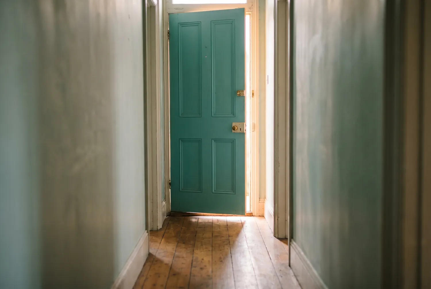 Morning light spilling through a teal front door standing slightly ajar at the end of a hallway Morning light spilling through a teal front door standing slightly ajar at the end of a hallway