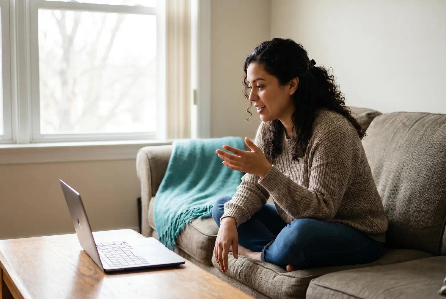 Woman on a sofa speaking naturally during a telepsychiatry video call, a teal blanket on the sofa arm Woman on a sofa speaking naturally during a telepsychiatry video call, a teal blanket on the sofa arm